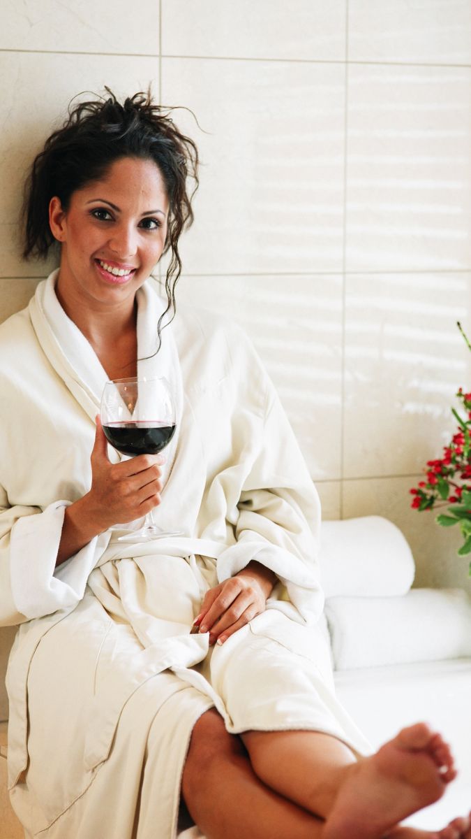 Woman in dressing gown with a glass of wine by a bath tub