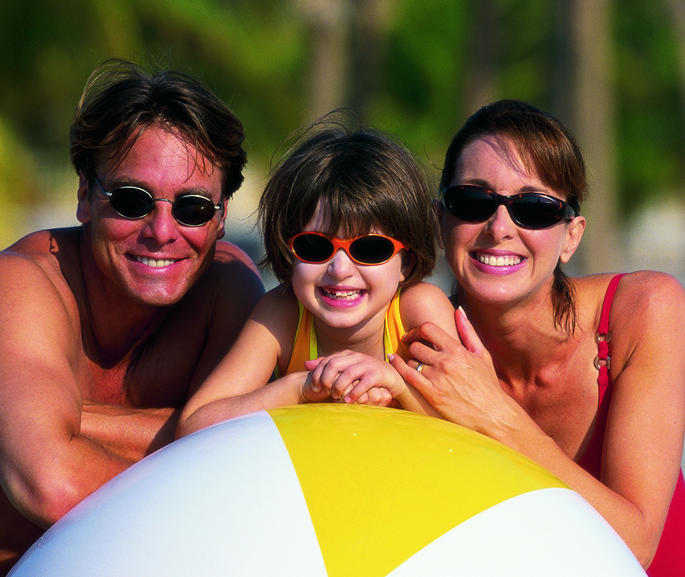 Mum, dad and daughter at teh beach leaning over a arge blow up beach ball